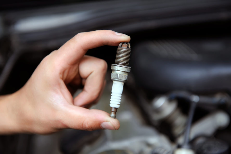 man holding a spark plug in front of a car engine