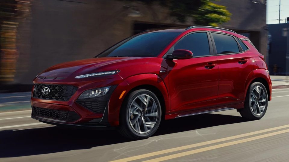 Red Hyundai Kona cruising down the street on a sunny day