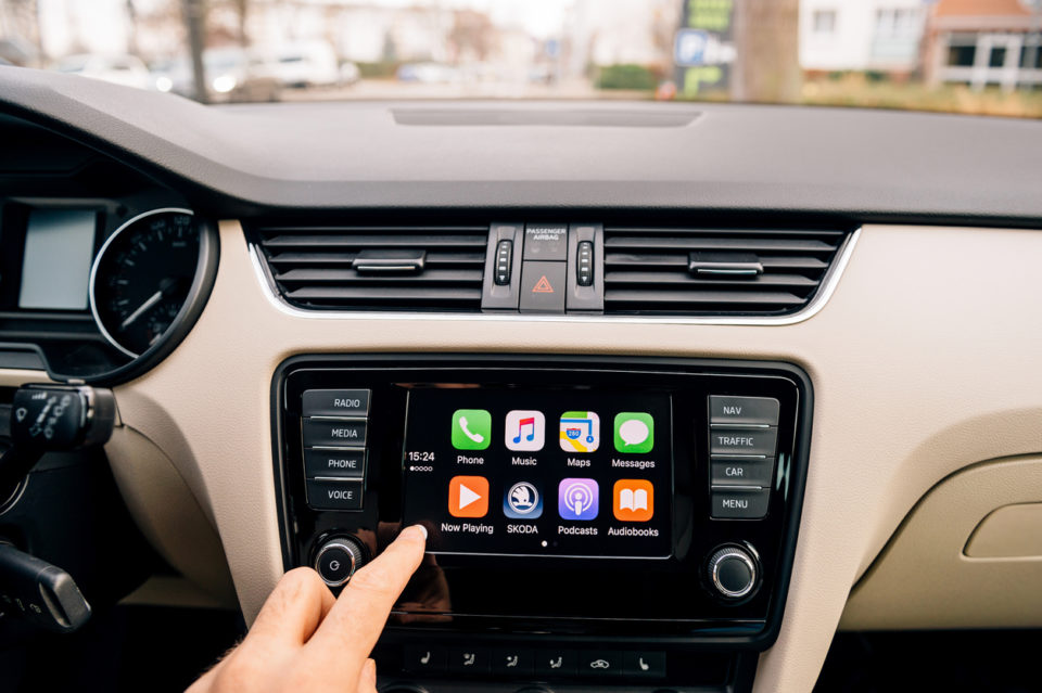 Man pressing home button on the Apple CarPlay main screen in modern car dashboard. CarPlay is an Apple standard that enables a car radio or head unit to be a display and controller for an iPhone.